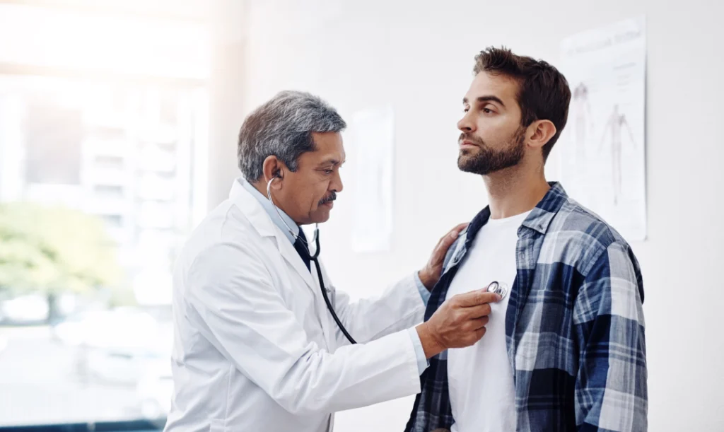 A physician using a stethoscope to examine a patient's chest during a primary care physical.