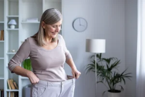 A happy older woman trying on oversized pants after significant weight loss with Wegovy.