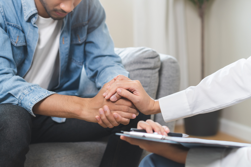 Counselor holding a man’s hand during a Mental Health Awareness Month consultation.