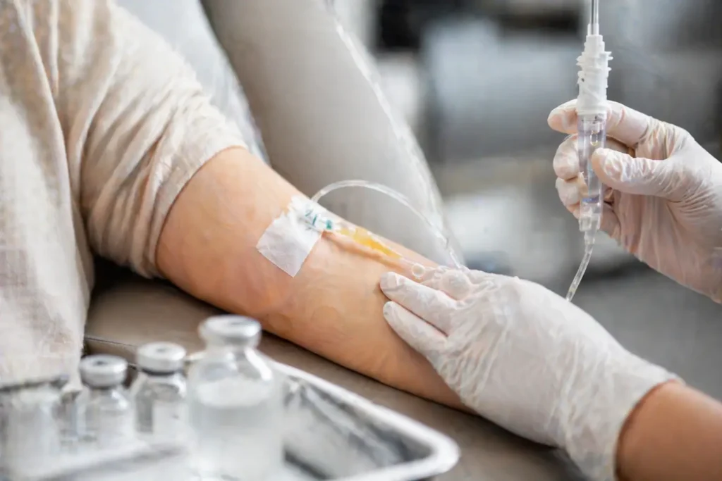 close-up of an arm with an IV line while a gloved hand adjusts tubing 