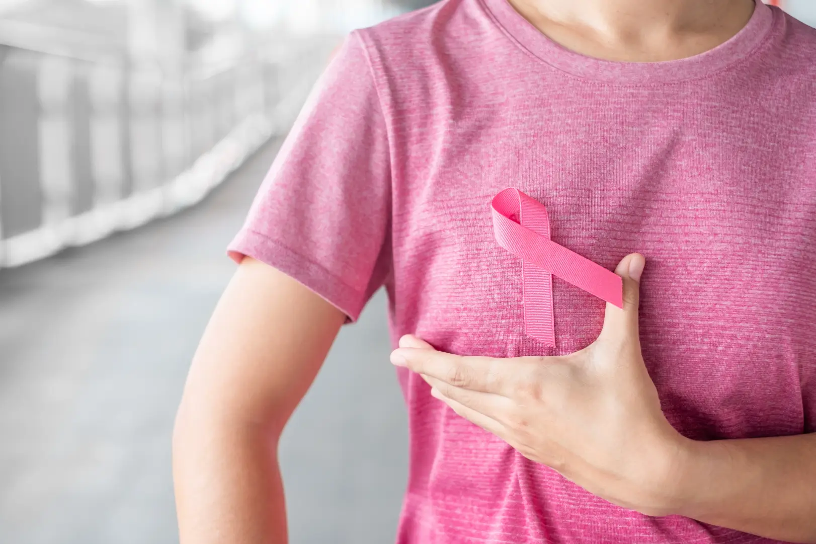 Person in a pink shirt holds a pink awareness ribbon against their chest.