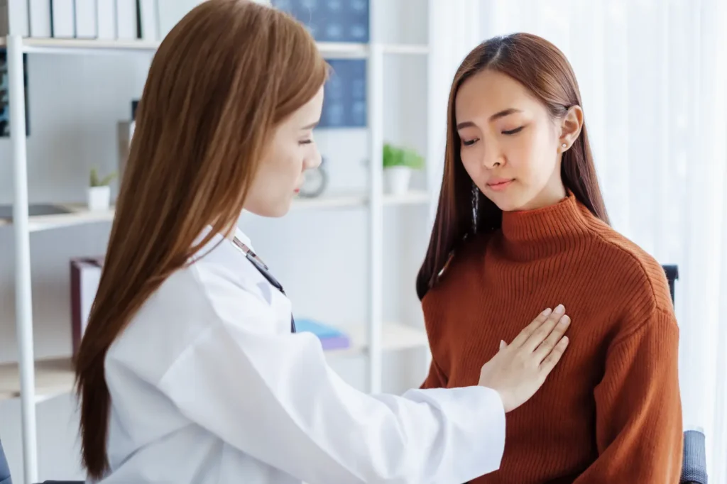 Doctor places a hand on a seated woman's upper chest during an examination in a medical office.