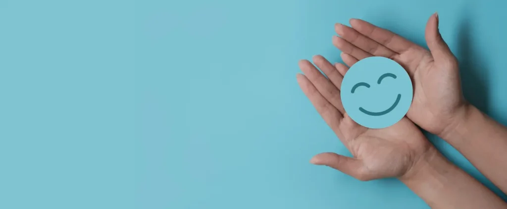 Two hands hold a blue circular card with a smiling face symbol against a matching blue background.